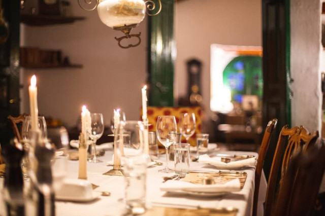 Candlelit dinner table with wine glasses in an antique-style dining room.