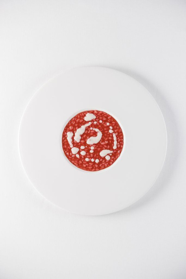 A white plate holds a circular slice of red salami with white fat specks, set against a plain white background