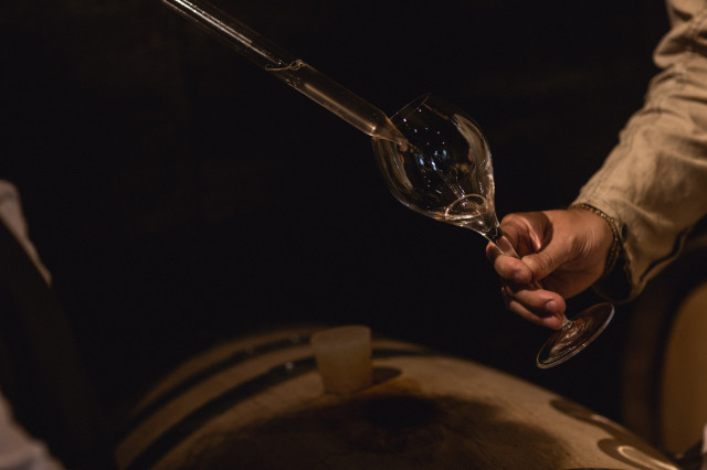 Liquid poured into glass near wooden barrel.