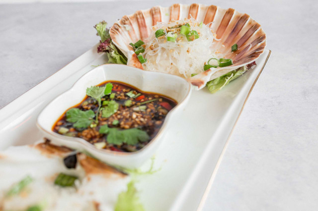 Scallop shell with noodles and sauce on a white platter.