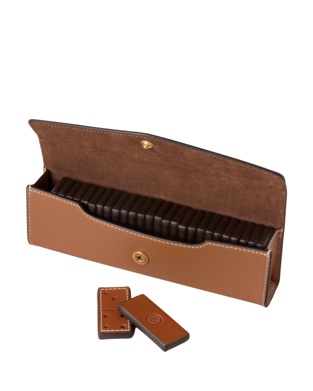 A leather case holds several rectangular chocolate bars, neatly stacked, with two bars placed in front on a white surface. The case is open, revealing a button clasp.