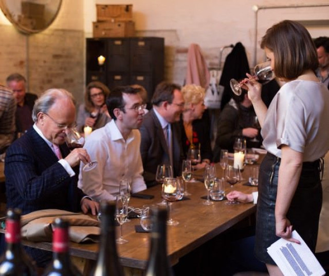 People seated around a wooden table engage in a wine tasting