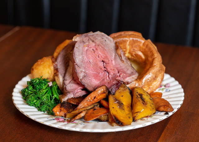 Roast beef with vegetables on a patterned plate.