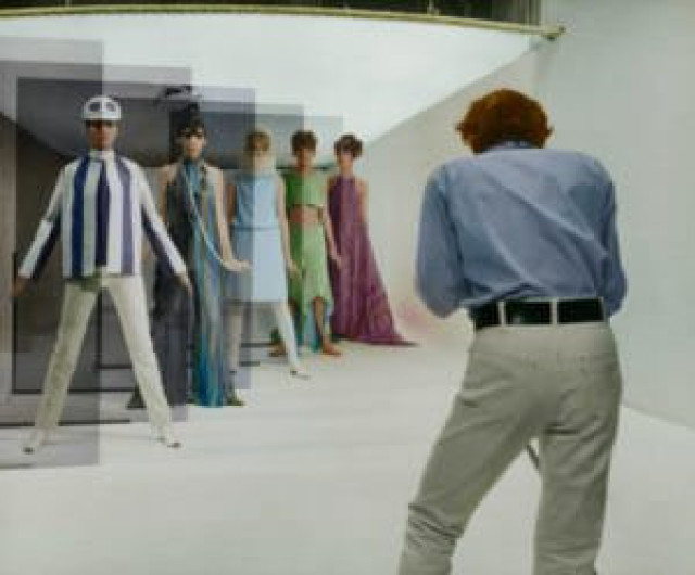 Man photographing mannequins in 1960s fashion in a studio.