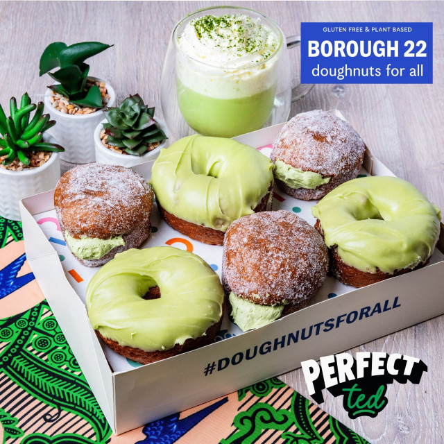 Doughnuts with green glaze or sugar coating are arranged in a box. A green beverage in a glass is nearby, surrounded by small potted plants. Text: 