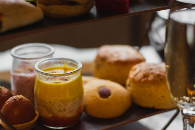 Dessert jars among pastries on a tiered tray with wine.