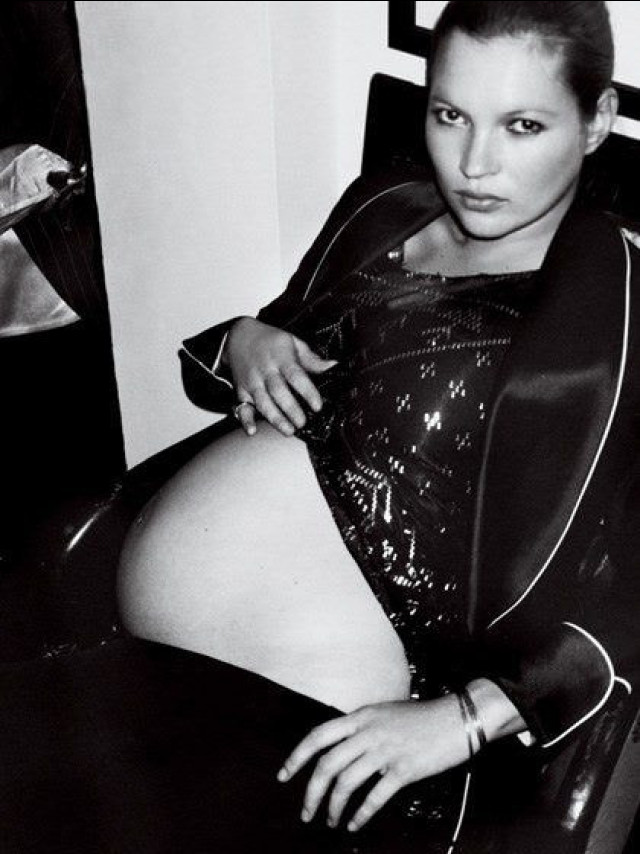 Pregnant woman in sequined top rests hands on her abdomen.