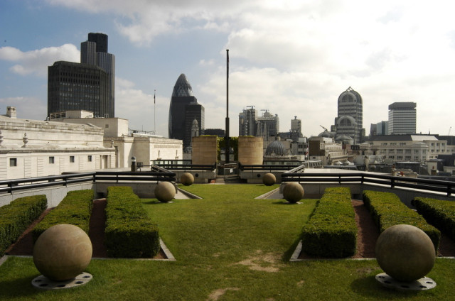 Large stone spheres rest on a rooftop garden with neatly trimmed hedges