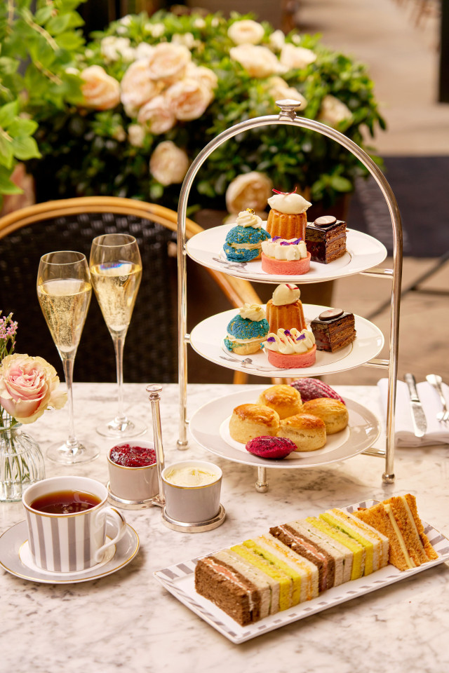 marble table featuring tiered cake stand, two glasses of fizz and finger sandwiches