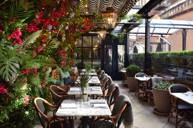 Tropical floral wall behind bistro tables in a glass-roofed patio.