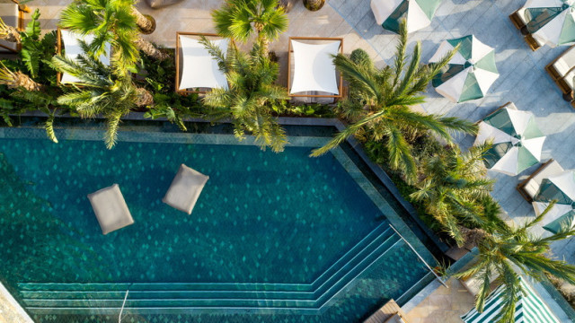 Teal pool surrounded by palm trees and cabanas.