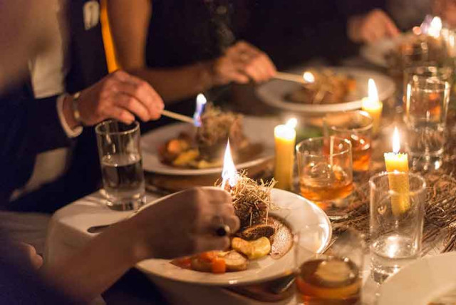 Diners enjoy a meal, lighting herbs on gourmet plates with candles