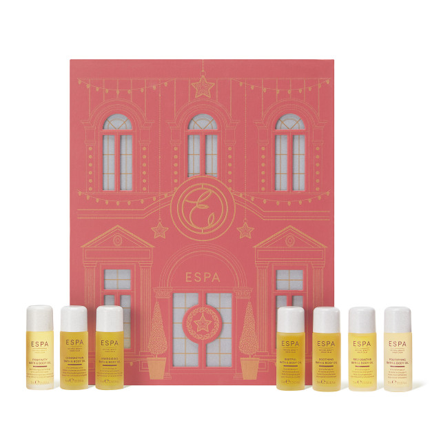 Bottles of ESPA skincare products stand arranged in front of a decorative pink box resembling a building façade, adorned with festive lights and geometric designs.