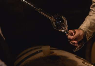 Liquid poured into glass near wooden barrel.