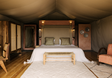 Bed inside canvas tent with wooden furniture.