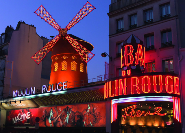 A brightly lit red windmill stands atop the Moulin Rouge building, surrounded by neon signs and vibrant lights against a twilight sky. Text includes: “Moulin Rouge,” “Ba du Moulin Rouge,” “Machine,” and “Féerie.”