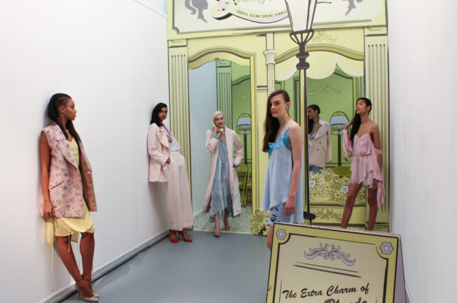 Models stand in a hallway posing amid pastel-colored outfits