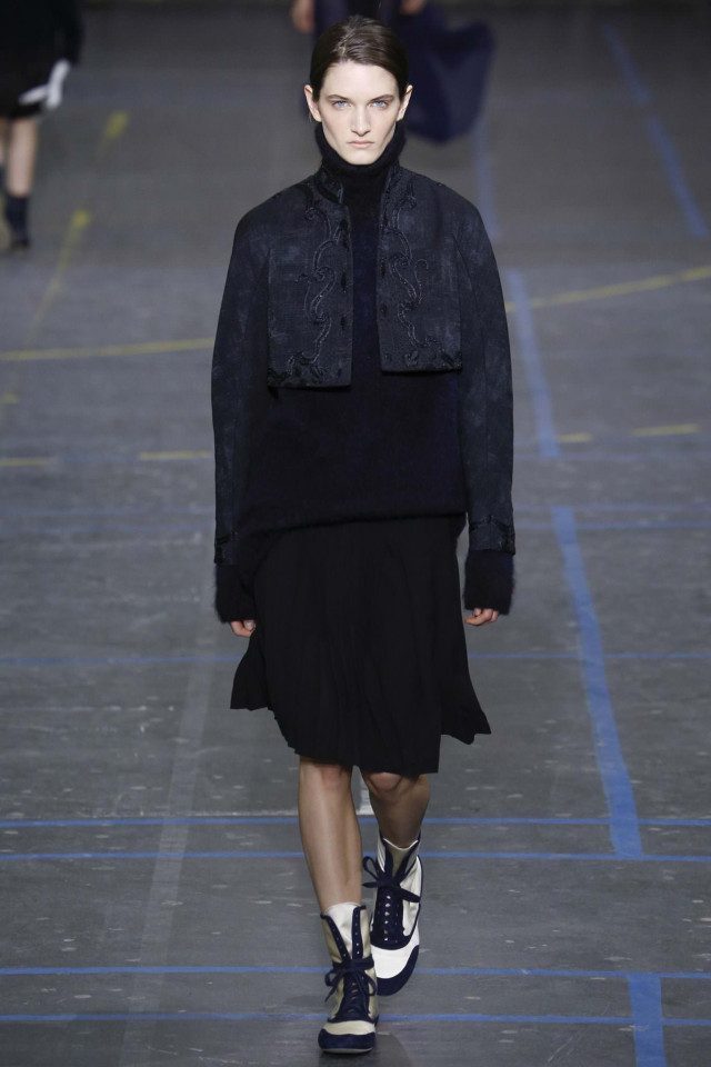 Woman modeling dark clothing on a runway.