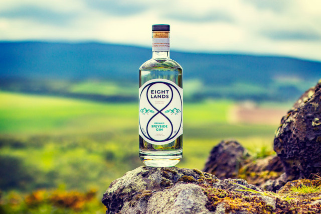 Eight Lands Organic Gin bottle on rock with hill backdrop.