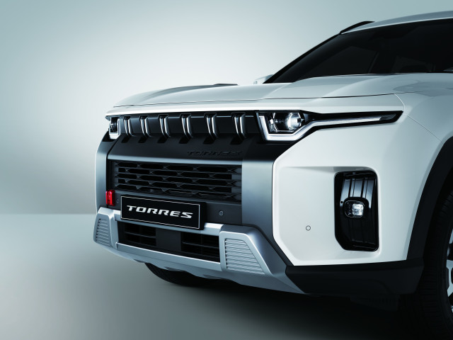 A white SUV is parked, showcasing its front grille and angular headlights, with the word 