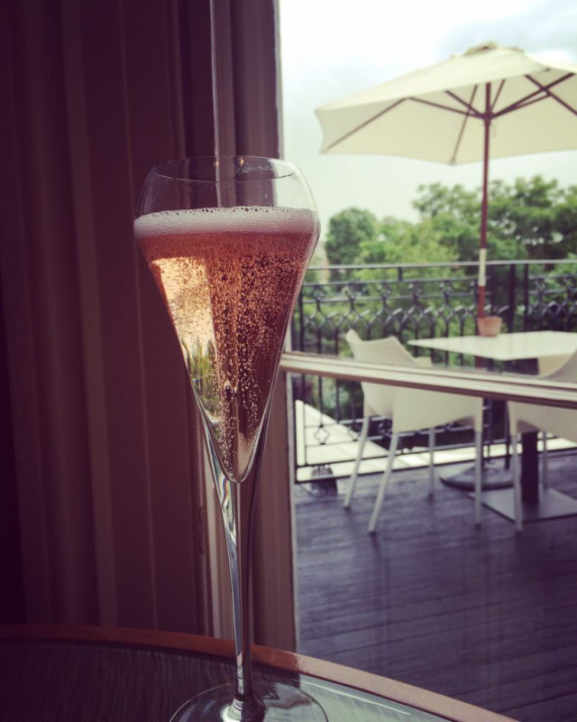 Champagne flute with rosé on a table; outdoor patio visible through a window.