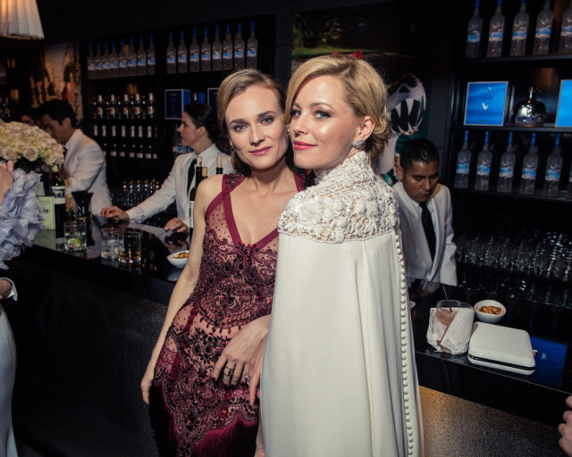 Two women in formal dresses posing at a bar.