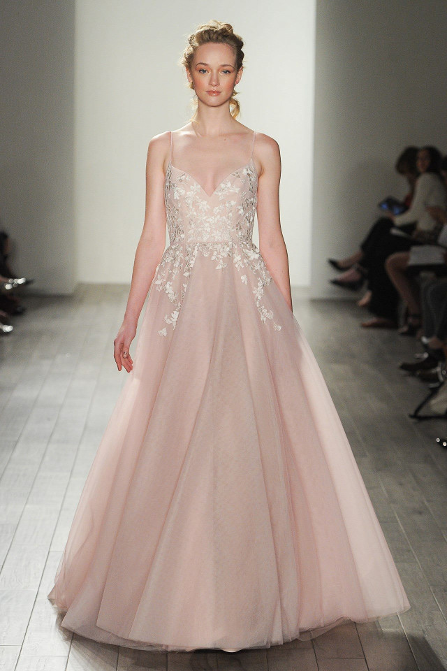 A model walks down a runway wearing a light pink, floral-embroidered gown