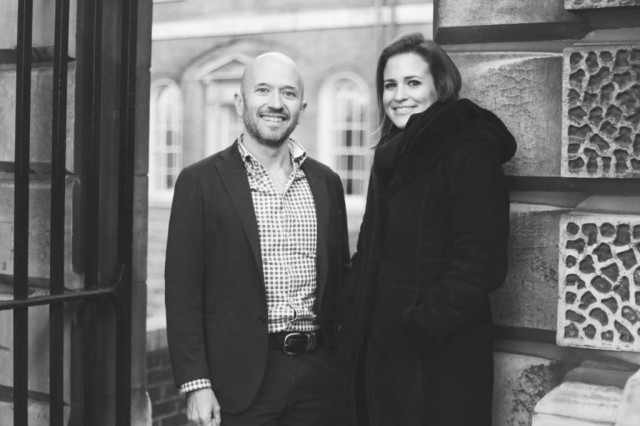 Two people stand smiling in a black-and-white photo