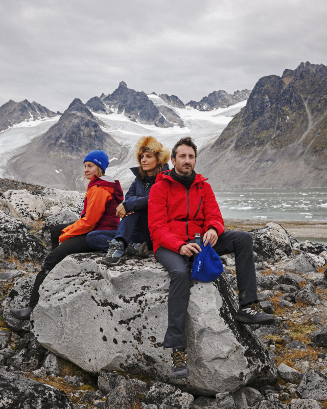 Three hikers resting by snowy mountains.