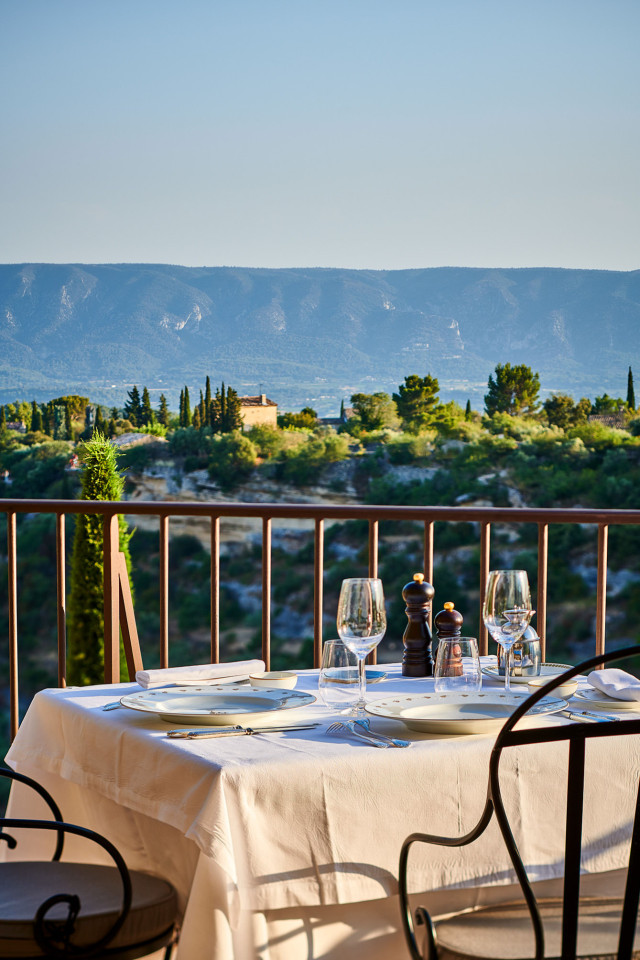 A table set with white tablecloth and glassware overlooks a scenic landscape of lush greenery and mountains under a clear blue sky