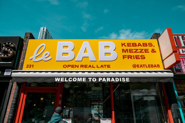 Yellow storefront sign for 'le BAB' advertising kebabs, mezze, and fries.