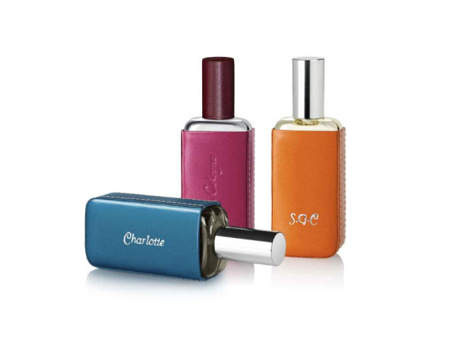 Three perfume bottles, each encased in colored leather with silver caps, are displayed