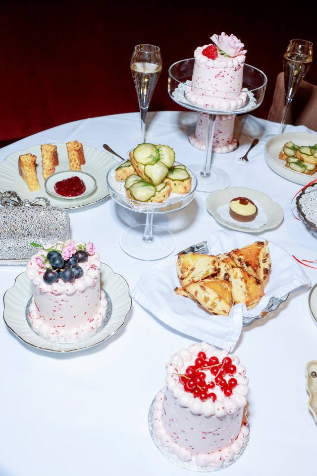 white table laid with cakes, afternoon tea dishes and glass of fizz