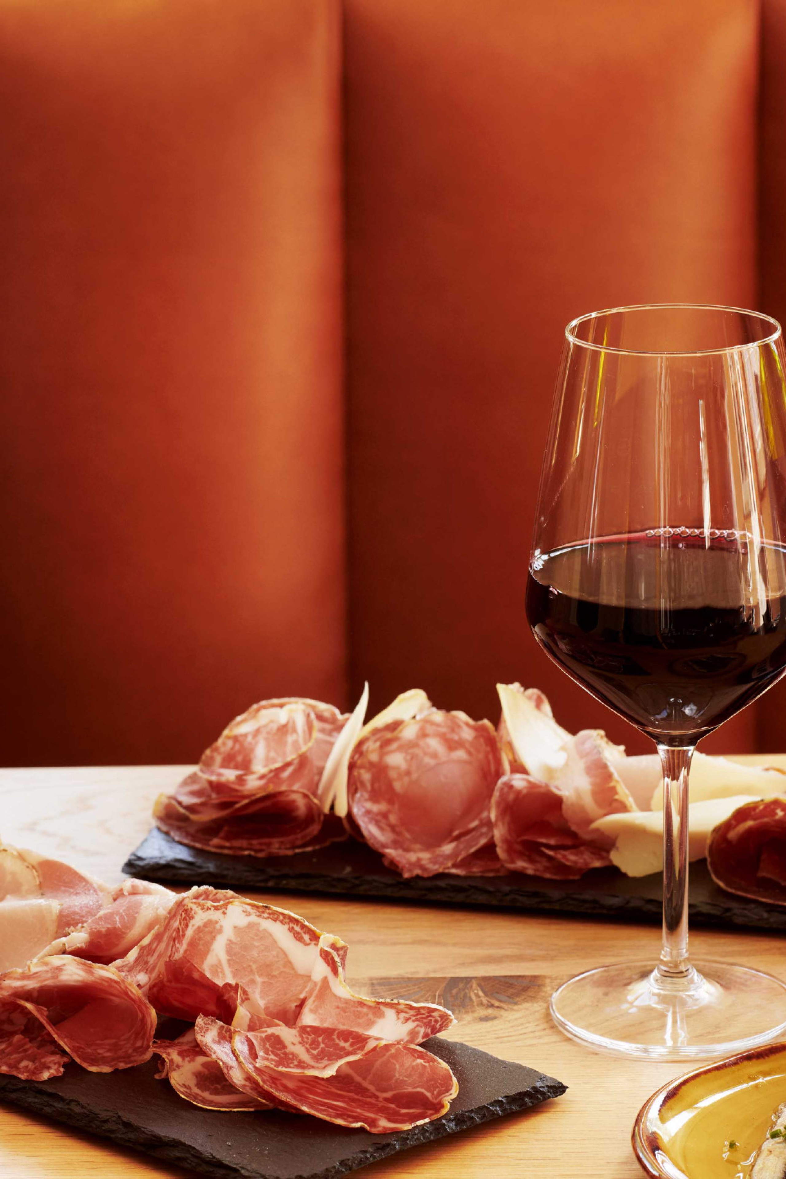 Two wine glasses filled with red wine, accompanied by a bottle labeled "METIC," sit on a wooden table