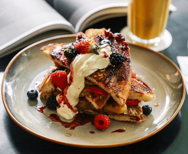 French toast topped with whipped cream and mixed berries rests on a plate