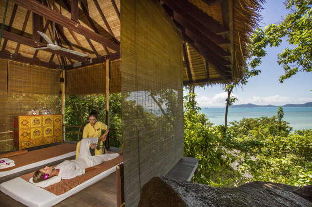 A therapist gently stretches a client's leg on a massage bed in an open pavilion