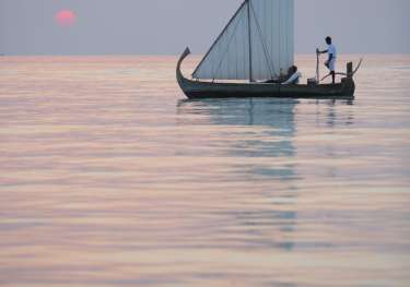 Sailboat during sunset with person at the helm.