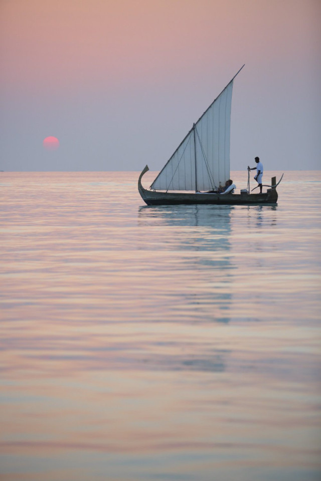 Sailboat during sunset with person at the helm.