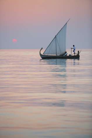 Sailboat during sunset with person at the helm.