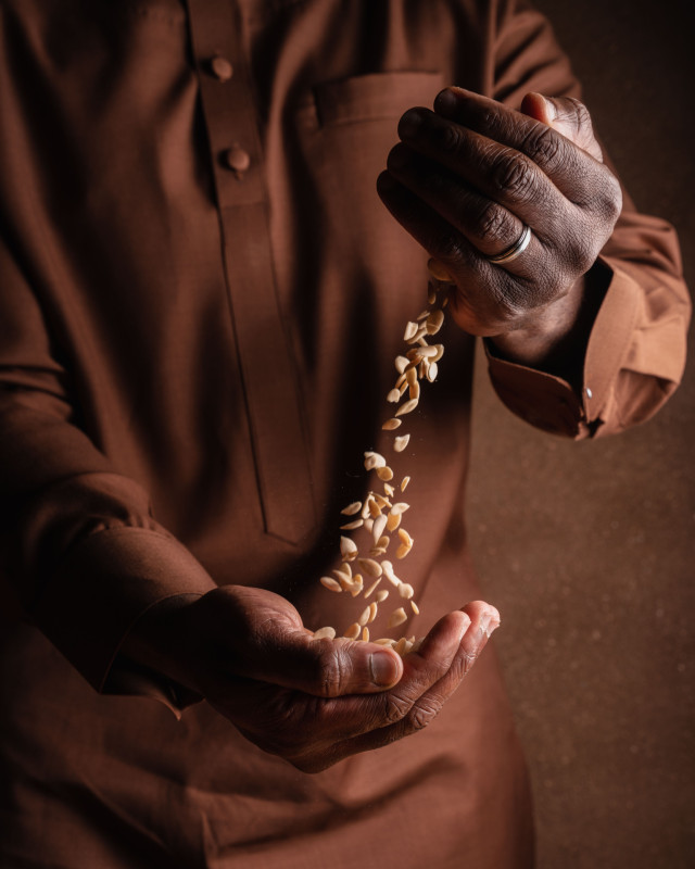 Hands pouring seeds from one palm to another, wearing a brown shirt, in a dimly lit setting