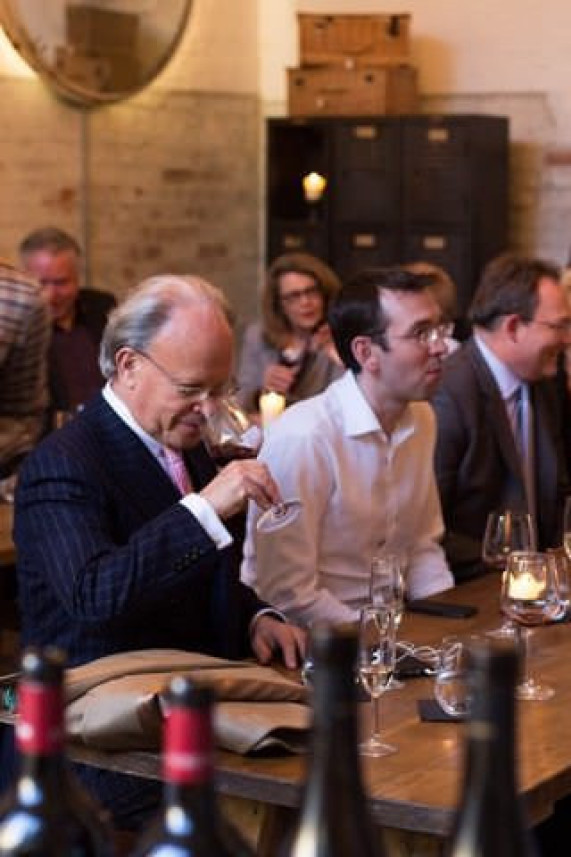 People seated around a wooden table engage in a wine tasting