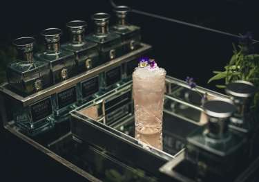 A cocktail glass with a floral garnish sits on a reflective tray.