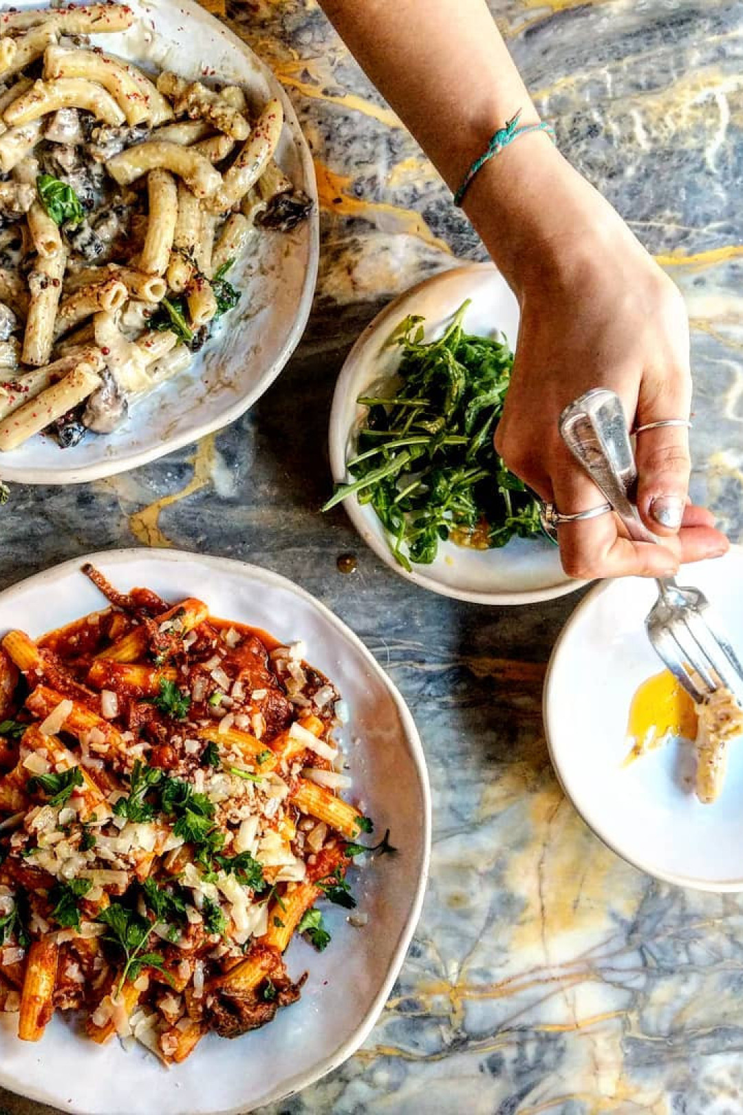Pasta dishes and salad on a marble table.
