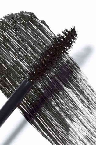A black mascara brush smears dark mascara across a white surface, showcasing the bristles and the texture of the applied product.