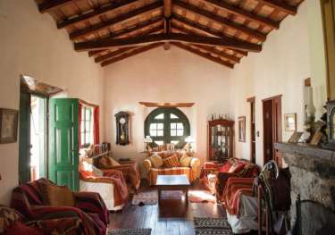 Rustic living room with couches, wood-beamed ceiling, and sunlight.