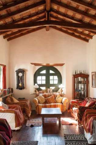 Rustic living room with couches, wood-beamed ceiling, and sunlight.