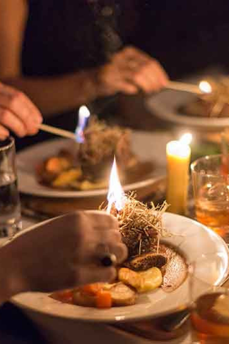 Diners enjoy a meal, lighting herbs on gourmet plates with candles