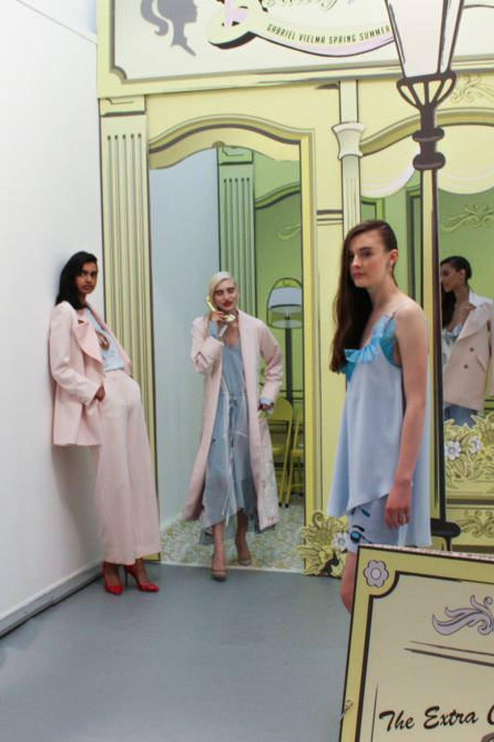Models stand in a hallway posing amid pastel-colored outfits