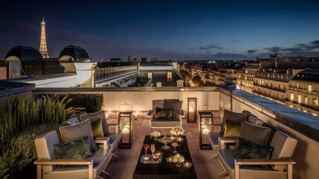 Elegant rooftop patio with chairs and tables adorned with drinks and flowers, softly lit by lanterns
