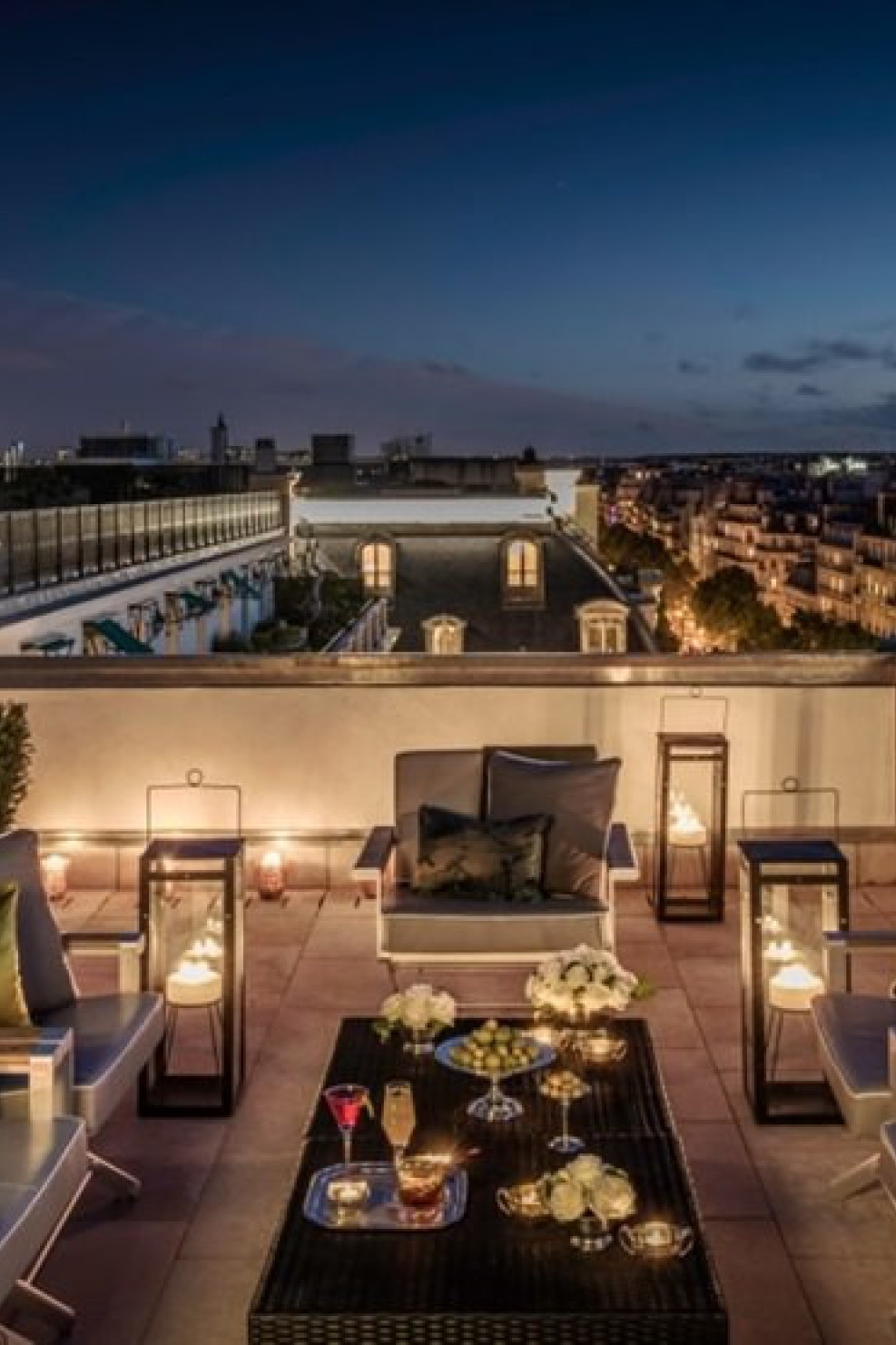 Elegant rooftop patio with chairs and tables adorned with drinks and flowers, softly lit by lanterns